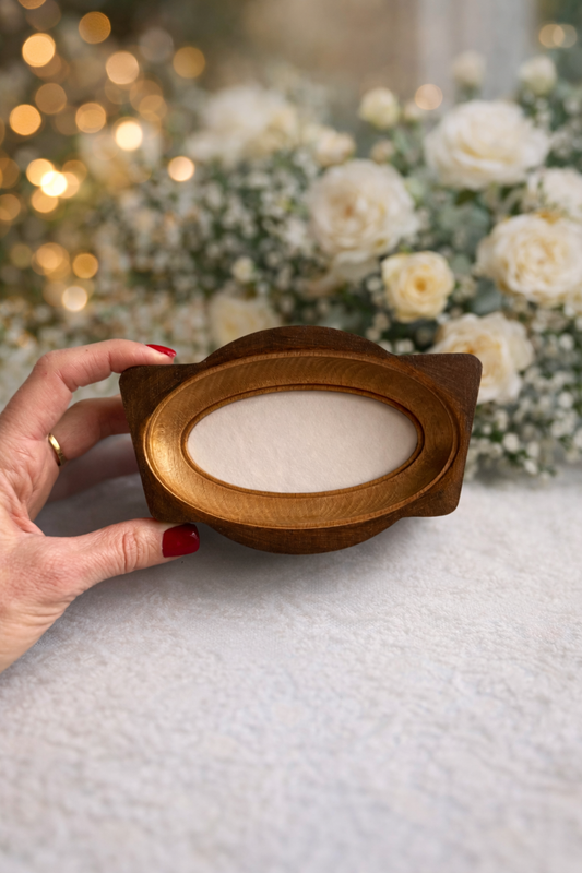 Wooden oval photo frame held by a hand against a floral background