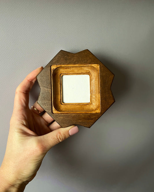 Hand holding a hexagonal wooden frame against a plain background