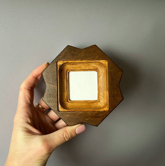 Hand holding a hexagonal wooden frame against a plain background