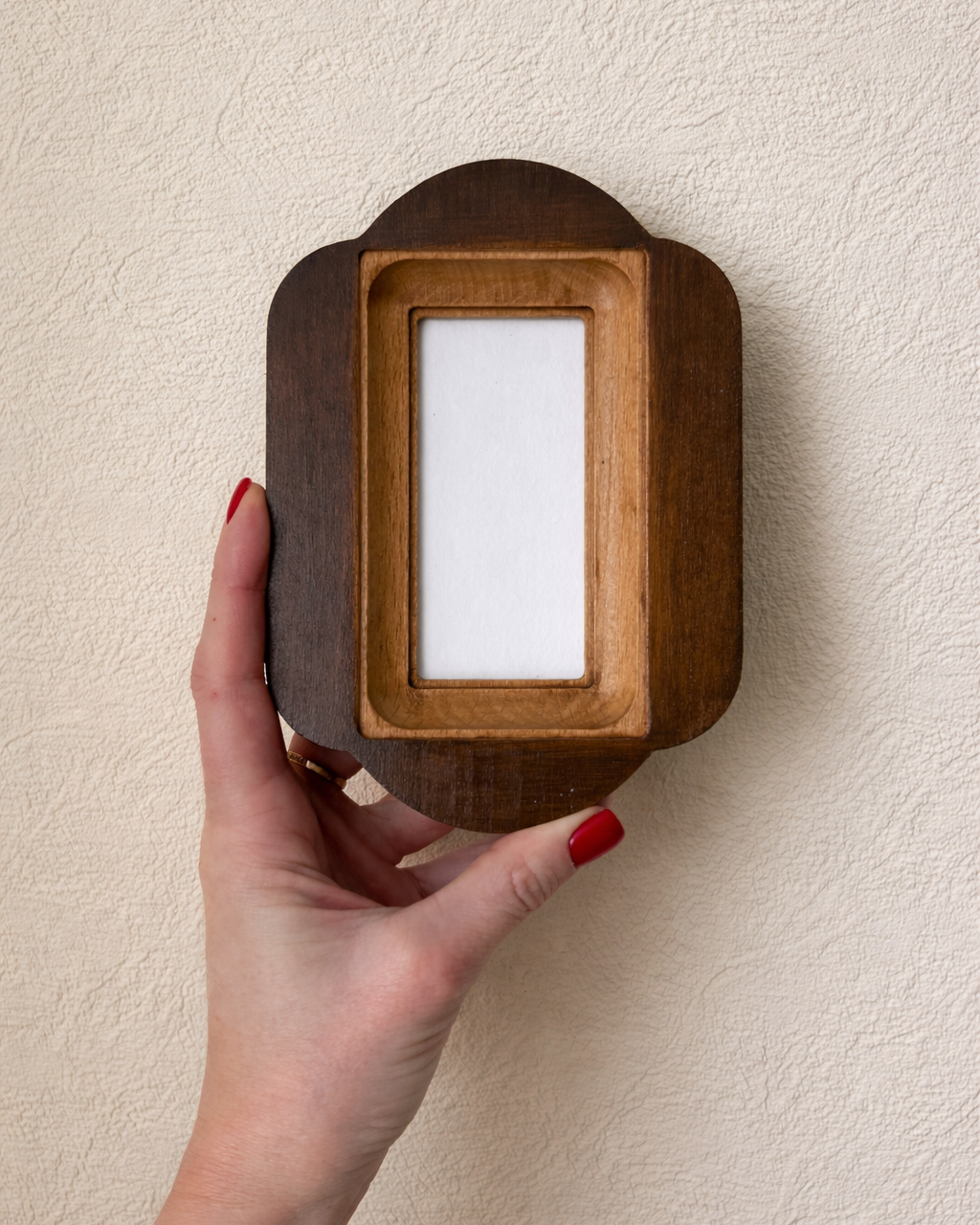 Wooden photo frame held by a hand against a beige wall