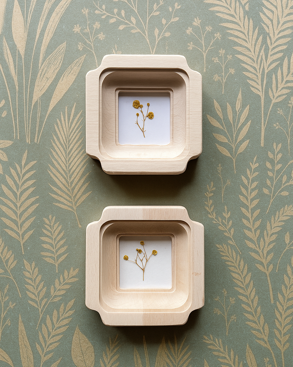 Two square wooden frames with small plants inside on a green background with leaf pattern