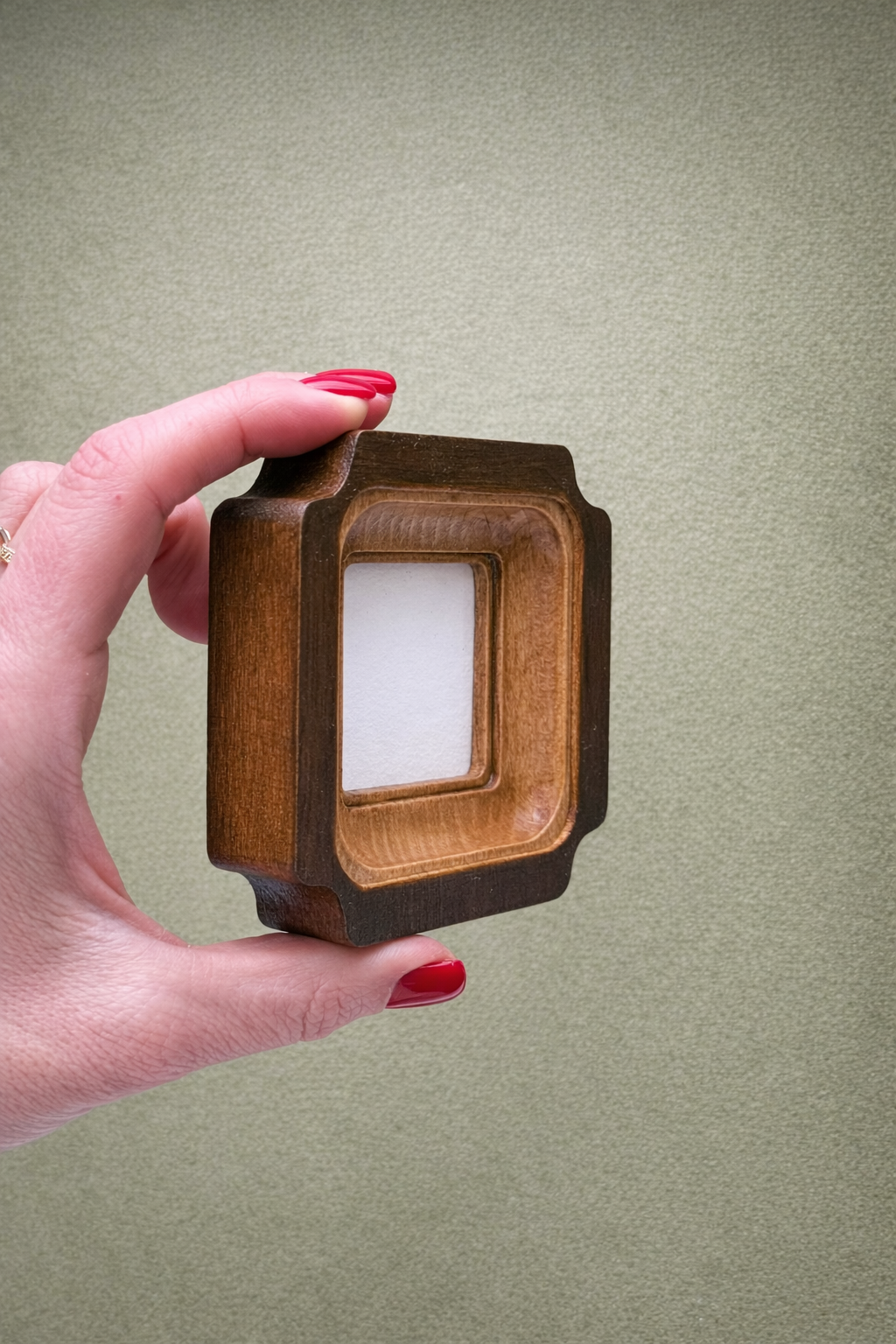 Hand holding a wooden frame with a white square inside against a beige background