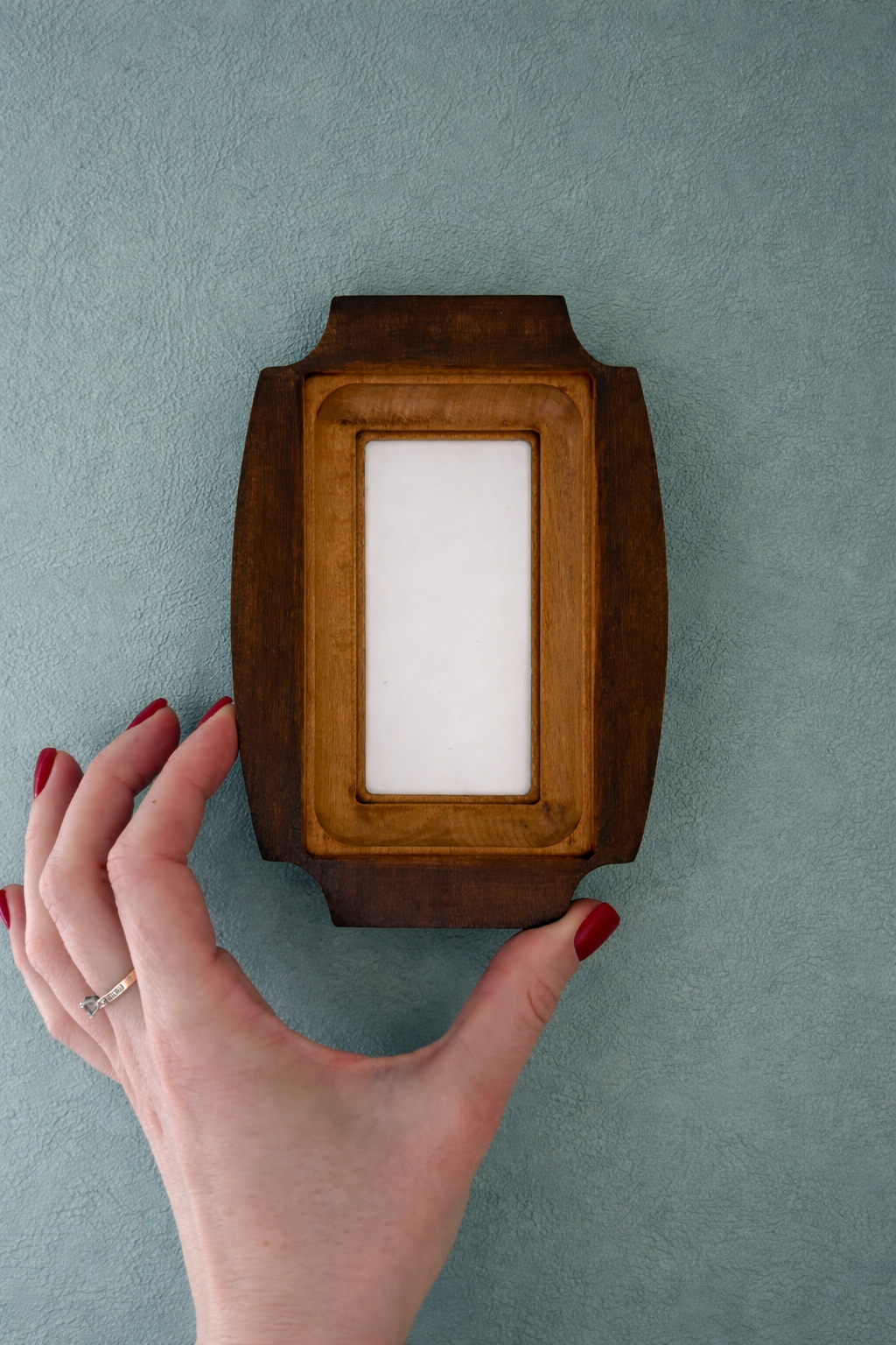 Wooden photo frame on a gray wall with a hand touching it