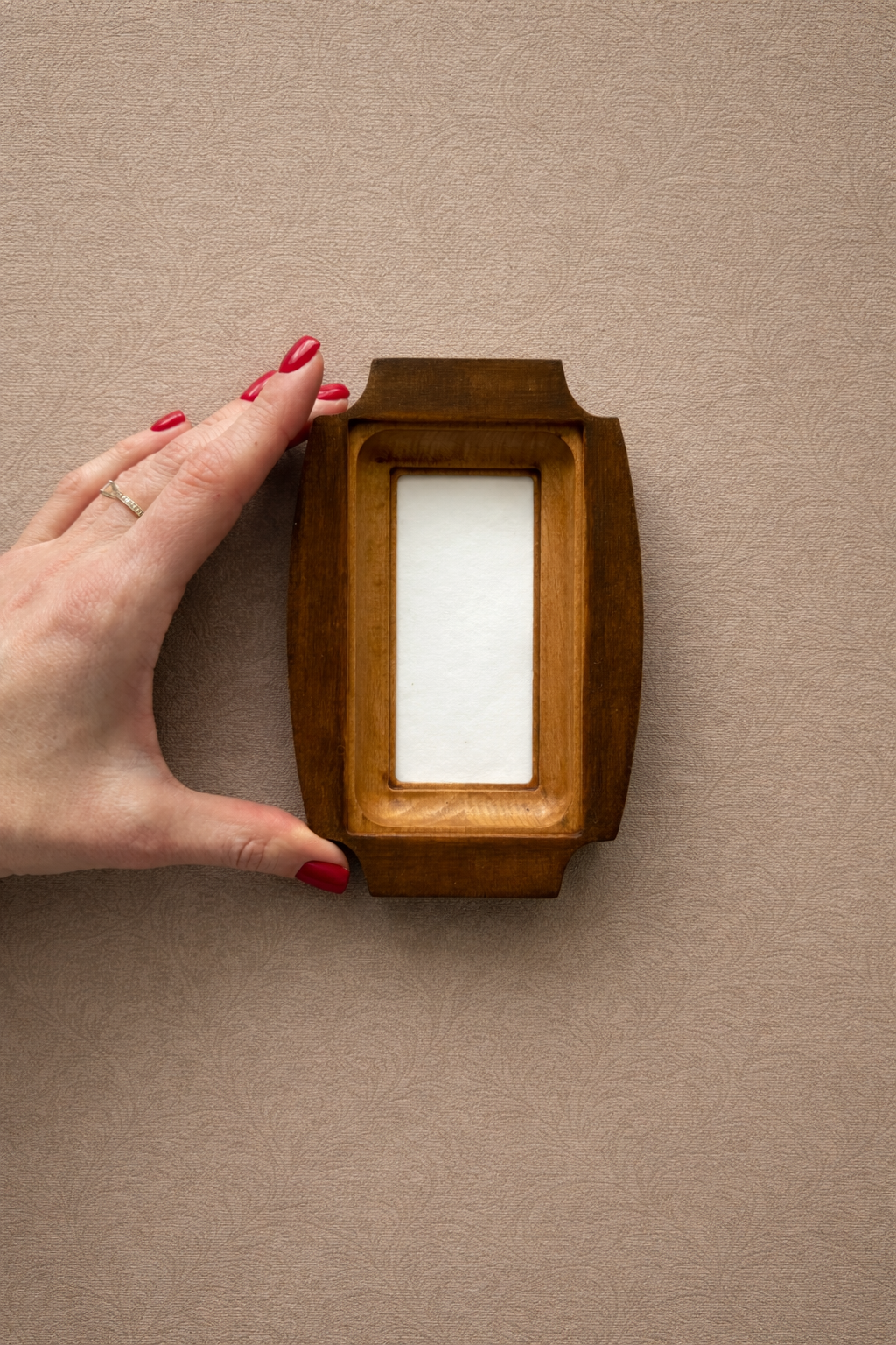 Hand holding a wooden frame with a white center against a beige background